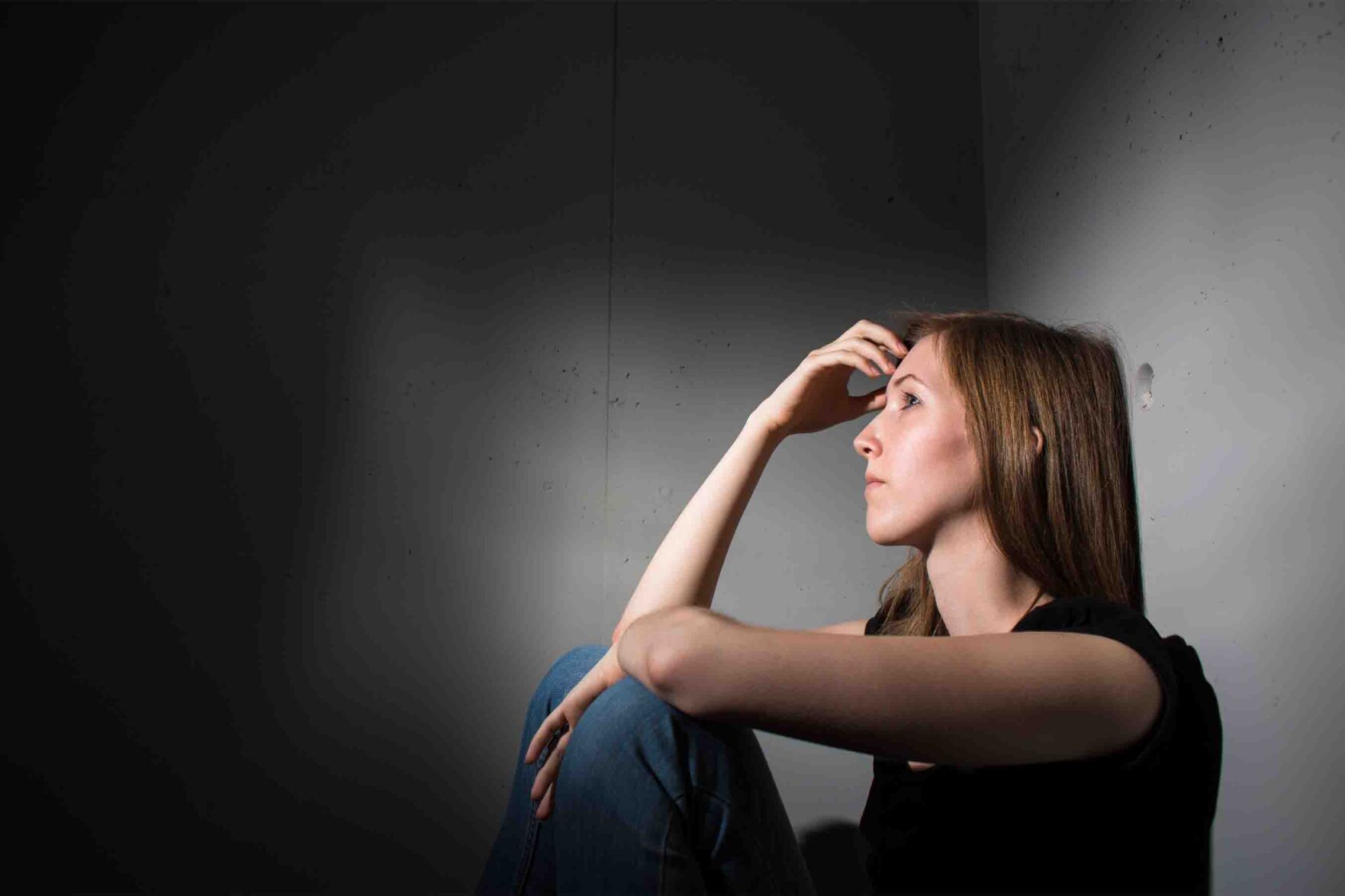 Young woman suffering from a severe depression (very harsh lighting is used on this shot to underline/convey the gloomy mood of the scene)